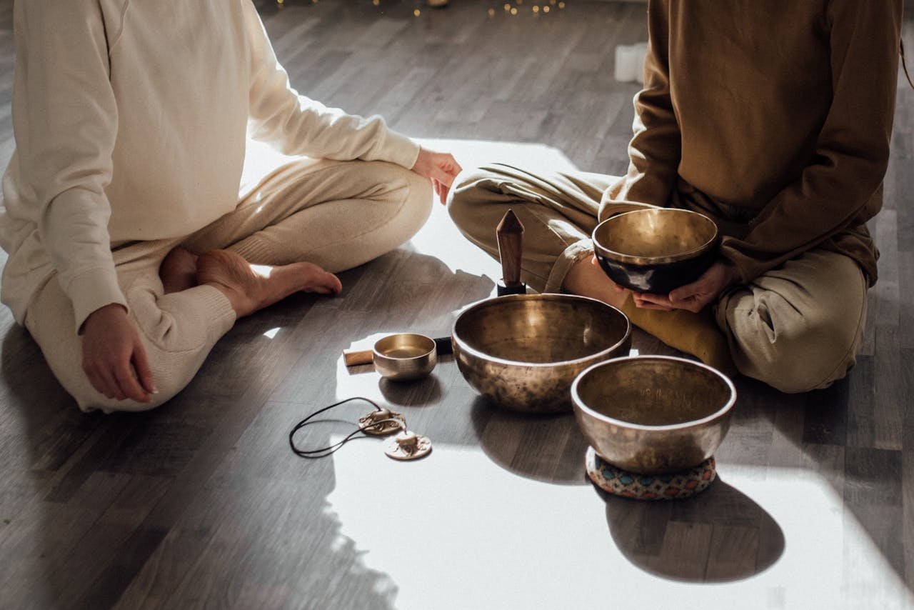 Two women meditating with Tibetan singing bowls in a serene indoor setting.